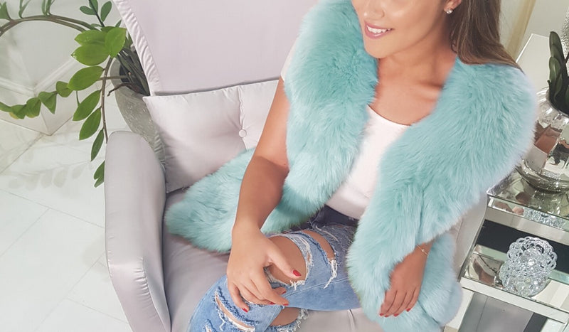 fashionable lady sitting in chair wearing ripped jeans and an amsterdam mint faux fur vest